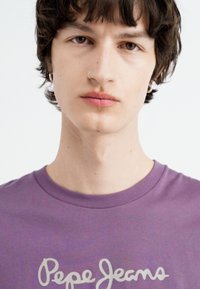 Violets kokvilnas t-krekls ar baltu "Pepe Jeans" tekstu, apaļu kakla izgriezumu un īsām piedurknēm. Gluda tekstūra ar minimālām rotājuma detaļām.