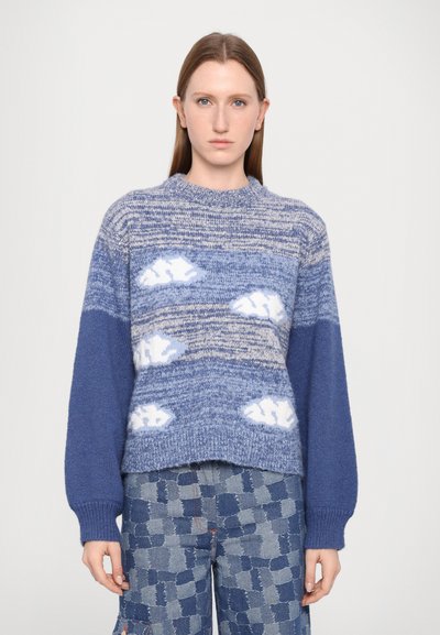 Pull tricoté bleu avec des nuances de bleu variées et des motifs de nuages blancs, un col rond et des poignets côtelés, associé à un pantalon à motifs.