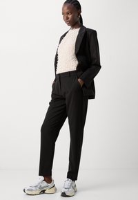 Mustra mustriga mustükk jacket tekstuuritud koorevärvi topi peal, mustade pükste ja hõbedaste sportlike kingadega. Minimalistlik disain ja neutraalne värvipalett.