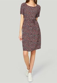 Punainen ja sininen kuvioitu lyhythihainen mekko pyöreällä pääntiellä, vyötäröltä laskostettu ja polvipituinen, yhdistettynä valkoisiin tennareihin.