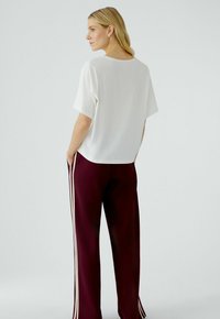 Witte blouse met korte mouwen gecombineerd met bordeauxrode broek met zijden witte strepen. De blouse heeft een ontspannen pasvorm met een ronde halslijn.