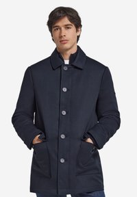 Marineblauer Mantel aus strukturiertem Stoff mit klassischem Kragen, sechs Knöpfen und Seitentaschen. Minimalistisches Design, gerade geschnitten.