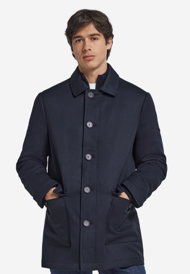 Marineblauer Mantel aus strukturiertem Stoff mit klassischem Kragen, sechs Knöpfen und Seitentaschen. Minimalistisches Design, gerade geschnitten.