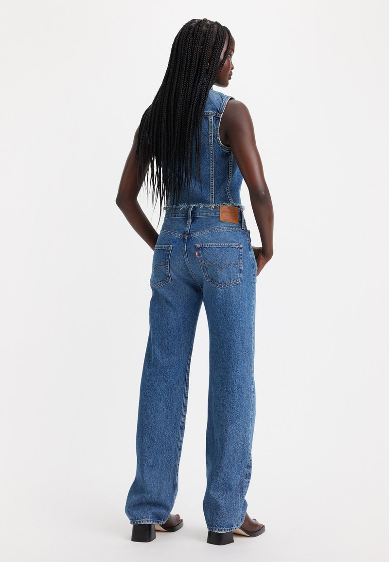 Denim-Minikleider in Mittelblau mit ärmellosem Design, weitem Bein, fransigem Saum und einem braunen Leder-Logopatch auf der Rückseite.