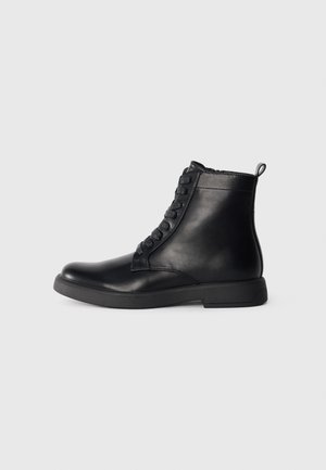Bottines en cuir noir avec un bout rond, un laçage frontal et un low block heel. Texture lisse et une languette à l'arrière.