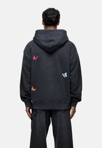 Felpa nera con cappuccio; presenta un ricamo colorato di farfalla nei toni del rosa, blu e arancione sul retro; realizzata in un morbido tessuto texturizzato.