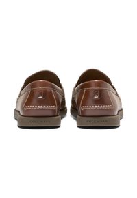 Mocassins en cuir marron vus de l'arrière, avec des coutures blanches et "COLE HAAN" embossé sur les semelles en caoutchouc tan.