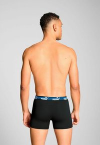 Black boxer briefs with a blue Puma logo waistband, featuring a snug fit and smooth texture, designed for comfort and flexibility.