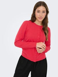 Czerwony kardigan z miękkiego materiału, z okrągłym dekoltem, długimi rękawami i guzikami z przodu. W połączeniu z czarnymi, luźnymi spodniami.