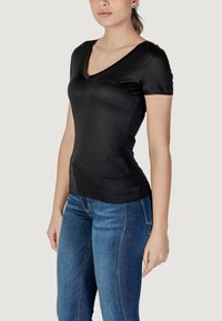 Sort tætsiddende t-shirt med V-udskæring, korte ærmer og glat tekstur, wedet med blå jeans med subtile stikningsdetaljer.