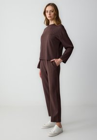 Bruine longsleeve top met studs, gecombineerd met bijpassende bruine broek en witte sneakers, met een ontspannen pasvorm en zakken.