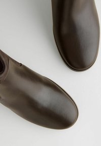 Bottes de cheville en cuir marron avec une texture lisse, bout arrondi et petit talon. Présente des coutures latérales et un design minimaliste.