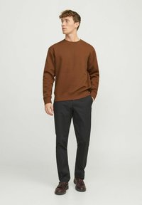 Sudadera marrón con cuello redondo, puños acanalados y corte recto, combinada con pantalones negros y zapatos oscuros. Diseño simple, colores sólidos.