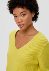 Geel geribd brei sweater met een V-halsontwerp. De stof lijkt zacht en gestructureerd, wat zorgt voor een aansluitende pasvorm rond de schouders.