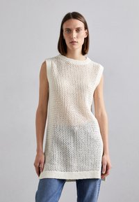Top senza maniche lavorato a maglia color crema, con una texture a trama larga ed orlo a coste. Abbinato a jeans blu per un look informale.