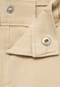 Yksivärinen beige kangas, jossa on teksturoitu twill-kudos, hopea neppari, kontrastiväriset ompeleet ja taitettu helma.