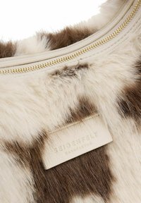 Sac en fausse fourrure présentant un mélange de teintes crème et marron, détaillé avec une fermeture éclair dorée et une étiquette en cuir texturé embossée avec "SEIDENFELT."