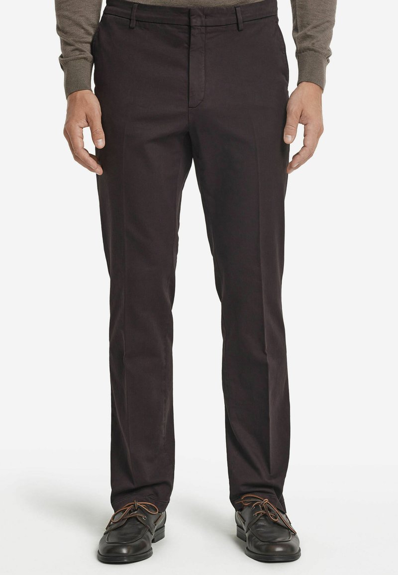 Mörkbruna bomullshängselbyxor med rak passform, som har sidofickor och platt front. Matchade med svarta skor med bruna snören.