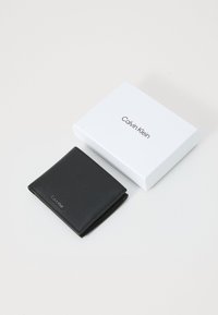 Schwarze Lederbrieftasche mit strukturiertem Finish, gefaltetes Design, das ein dezentes Calvin Klein-Logo zeigt. Wird mit einer weißen, gebrandeten Geschenkbox geliefert.