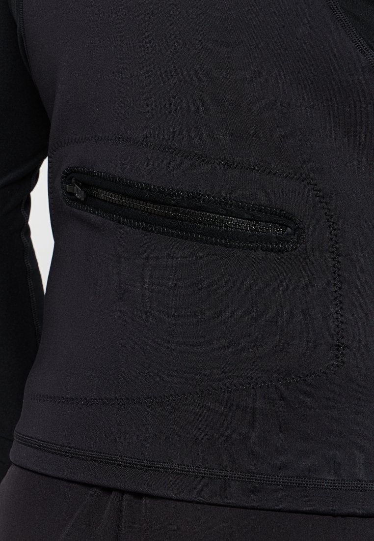 Czarny sportowy top wykonany z gładkiego, elastycznego materiału z poziomą kieszonką na suwak oraz płaskimi szwami, które zmniejszają objętość.