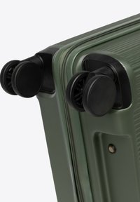 Zelený tvrdý kufr s dvojitými černými kolečky a viditelným zipem podél okraje na bílém pozadí.