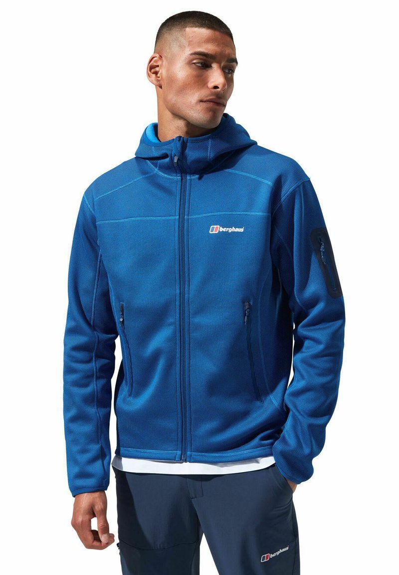 Blaue Fleecejacke mit Reißverschluss, strukturiertem Stoff, verstellbarer Kapuze und zwei Seitentaschen. Mit Logo auf der Brust und einer Tasche am Ärmel.