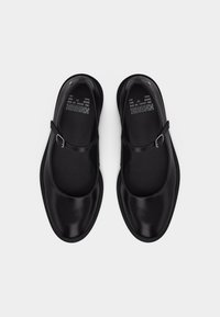 Μαύρα παπούτσια Mary Jane με λουράκια και αγκράφες, με στρογγυλεμένες μύτες, φωτογραφημένα από πάνω σε λευκό φόντο.