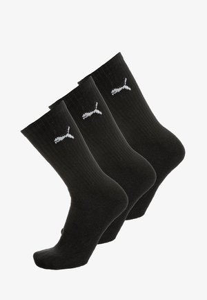 Trzy pary czarnych skarpetek crew z białym logo Pumy na kostce, wyeksponowane w przesuniętym układzie.