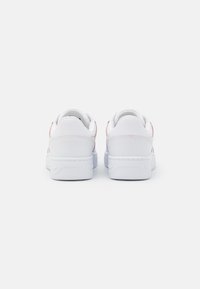 Bílé tenisky s hladkou, matnou texturou. Zaoblený tvar s jemnými růžovými akcenty na patě a polstrovaným límcem. Gumená podrážka.