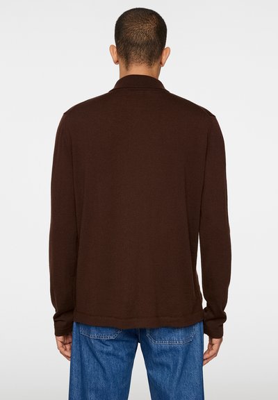 Polo shirt marrone a maniche lunghe con colletto a coste, texture liscia e orlo dritto, abbinato a jeans in denim blu.