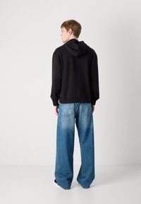 Black hooded sweatshirt with a relaxed fit and ribbed cuffs, paired with light blue wide-leg denim jeans featuring back pockets and fading.