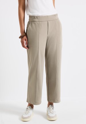 Beige hochtaillierte weite Hosen mit einem elastischen Bund, ausgestattet mit vorderen Taschen und gesteppten Details, kombiniert mit weißen Sneakers.