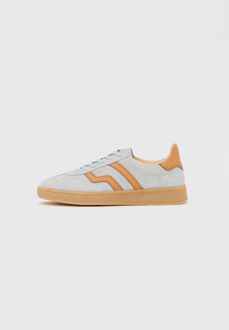 Hellgrauer Wildledersneaker mit cognacfarbenen Lederakzenten, Gummisohle und hellblauen Schnürsenkeln, von der Seite vor weißem Hintergrund gezeigt.