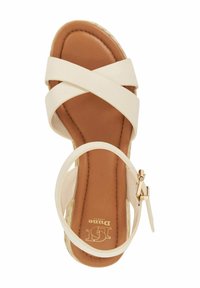 Cr�ème-kleurige sandalen met hak en gekruiste banden, een bruine voetbed en een gouden gesp op de enkelband. Geweven platformdetail zichtbaar.