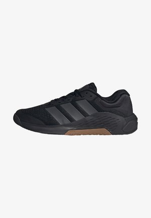 Zapatilla deportiva negra de corte bajo con parte superior de malla, tres franjas oscuras en el lateral, cierre de cordones y suela marrón texturizada.