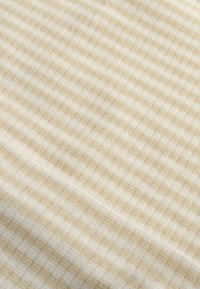 Béžová látka so štvorcovým vzorom, ktorý strieda svetlé a mierne tmavšie štvorce, mäkká textúra, ľahký a priedušný materiál.