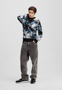 Sweater med et blåt, sort og hvidt abstrakt mønster, rund halsudskæring, parret med grå baggy jeans og sorte sneakers med blå accenter.