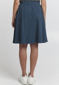 Jupe en denim bleu foncé avec un design évasé, taille élastique et longueur genou. Associée à des baskets blanches pour un contraste.