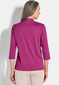 Fuchsia driekwart mouw top met een ronde halslijn. Glad stoftextuur, geen zichtbare patronen en een rechte snit.