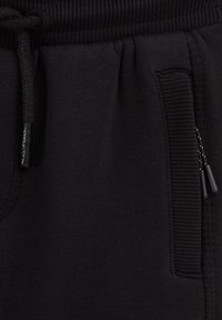 Mustad püksid on varustatud soonelise vöökohaga ja nööri, küljetaskuga, millel on tõmblukk, ning sileda tekstuuriga.