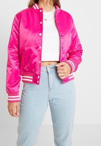 Bright pink satin bomber jacket with white and pink striped ribbed cuffs and collar, featuring snap buttons and a relaxed fit.