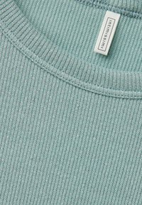 Licht teal geribbeld stof met een subtiele glans, voorzien van een ronde halslijn en een klein merklabel. De textuur is zacht en rekbaar.