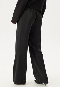 Zwarte wijde broek met een gladde, licht glanzende textuur. Elastische tailleband, geen zichtbare zakken en een ontspannen pasvorm.