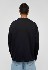 Zwarte sweatshirt met een relaxte pasvorm, ronde halslijn en verlengde schouders. Gladde textuur, ribgebreide cuffs en zoom. Lichtblauwe jeans.