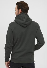 Sudadera con capucha de color gris oscuro, con un tejido resistente y puños y dobladillo acanalados. La parte posterior presenta un diseño clásico sin logotipos ni patrones visibles.