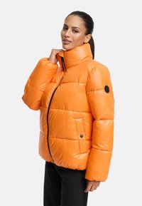 Fodrad jacka i stark orange, med hög krage, dragkedjestängning och sidofickor. Slät, glänsande yta med ett kviltat mönster.