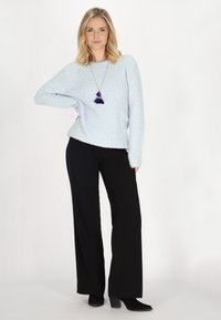 Pulover moale, de culoare albastru deschis, cu mâneci lungi, asortat cu pantaloni negri, largi. Modelul poartă un colier cu un accent dintr-o ciucure albastru.