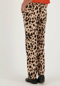 Beige en zwarte broek met luipaardprint, gemaakt van soepel materiaal, met een straight leg ontwerp en zijzakken. Zwarte schoenen gedragen.