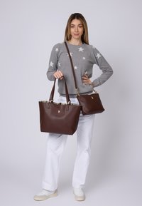 Borsa tote in pelle marrone con una finitura testurizzata, due manici superiori, hardware dorato e foderatura a scacchi. È mostrata anche una borsa più piccola coordinata.