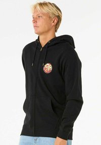 Sort zip-up hættejakke med et cirkul�ært farverigt grafisk design på brystet, snore til hætten og forlommer. Lavet af blødt stof med en glat overflade.